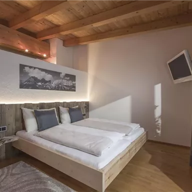 A modern bedroom with a double bed and wooden floor. Large windows and a cozy atmosphere create an inviting living space.