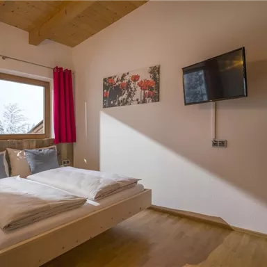A cozy bedroom with a large bed and two windows. A television and a colorful picture hang on the wall.
