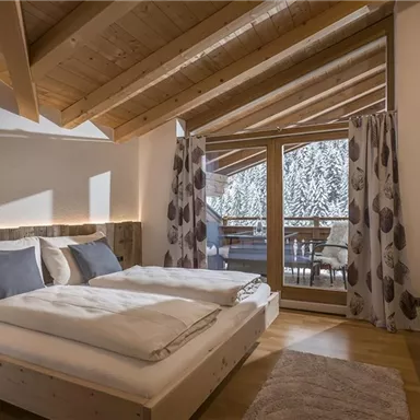 A modern bedroom with two single beds and cozy decor. Large windows offer views of a balcony and nature.
