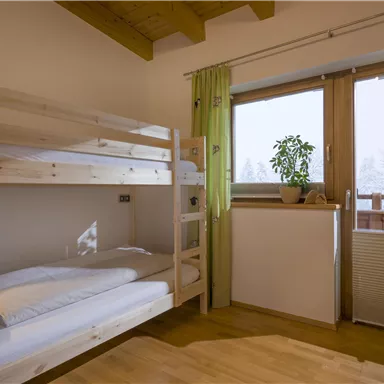 A bright bedroom with a loft bed and a large window.  
Plants create a pleasant atmosphere.