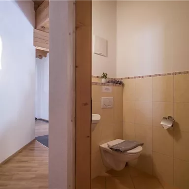 A small, clean bathroom with bright tiles. On the left is a toilet and on the right is a urinal, next to it is a towel.