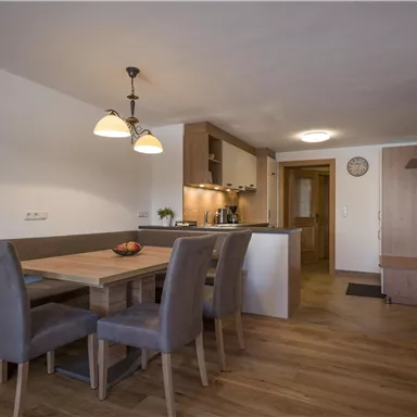 Ein modernes Esszimmer mit einem Holztisch und vier Stühlen. Die Küche ist offen und gut ausgestattet.