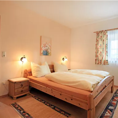 A cozy bedroom with a double bed and two nightstands. Soft colors and bright window decorations create an inviting atmosphere.