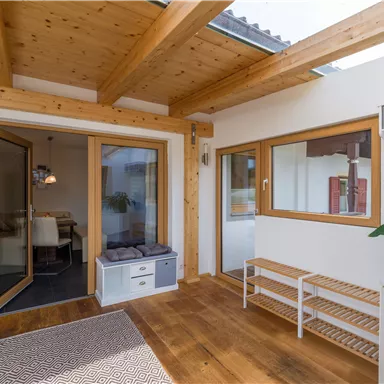 A bright and inviting interior with wooden beams and large windows. The room has a modern, minimalist style and provides access to another room.
