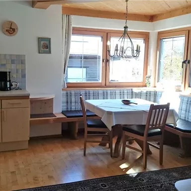 A bright kitchen with wooden shelves and a dining table. Large windows provide plenty of natural light.