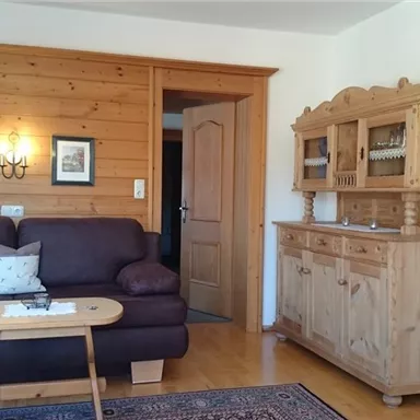 A cozy living room with a brown sofa and a wooden table.
On the wall, there are wooden panelings and picture frames, as well as a wooden sideboard.
