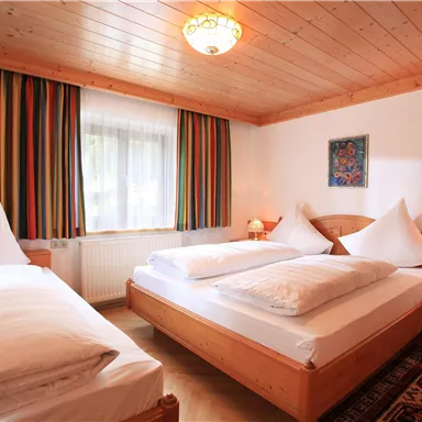 A cozy bedroom with two beds and an additional single bed. The room features wooden details and colorful curtains that create an inviting atmosphere.
