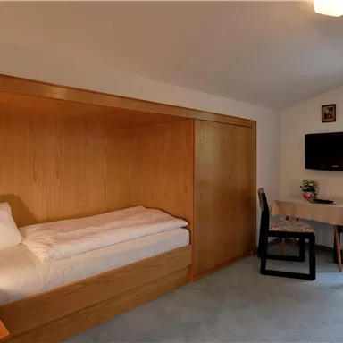 Ein einfaches Zimmer mit einem Bett, einem Tisch und zwei Stühlen. Es gibt einen Fernseher und ein Fenster mit Aussicht.