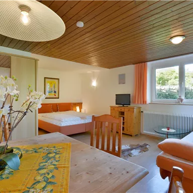 A cozy room with a dining area, a sofa, and a double bed. Large windows let in plenty of daylight.