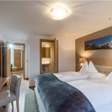 Ein modernes Hotelzimmer mit zwei Einzelbetten und stilvollem Dekor. Im Hintergrund ist ein Bild von Bergen zu sehen.