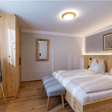 A modern bedroom with wood decor and two beds. The room is bright and cozy and features a television and a mirror.
