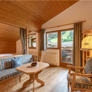 Ein gemütliches Zimmer mit Holzdecke und ansprechender Einrichtung. Die Fenster bieten einen Blick auf eine grüne Landschaft.