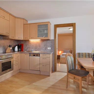 Eine moderne Küche mit Holzmöbeln und einem Essbereich. Die Ausstattung umfasst einen Herd, einen Kühlschrank und genügend Stauraum.