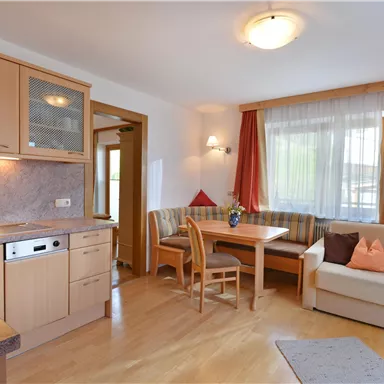 Eine gemütliche Wohnküche mit einer kleinen Essecke und einem bequemen Sofa. Die großen Fenster lassen viel Licht herein und schaffen eine einladende Atmosphäre.