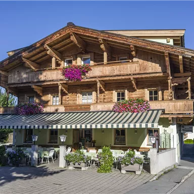 Ein traditionelles alpenländisches Haus mit Holzverzierungen und blühenden Blumen. Die Terrasse bietet Platz zum Entspannen und Genießen der schönen Landschaft.