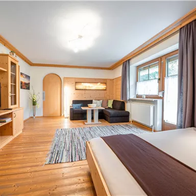 Ein gemütliches Zimmer mit Holzdetails und einem großen Fenster. Es gibt ein Bett, eine Sitzecke und einen Fernseher.