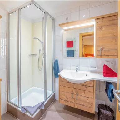 Ein modernes Badezimmer mit einer dusche und Holzschränken. Das Waschbecken ist hell und gut beleuchtet.