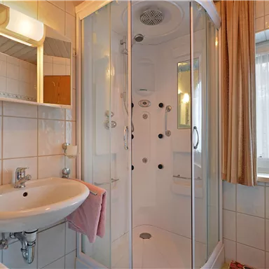 Ein Badezimmer mit einer modernen Dusche und einem Waschbecken. Helle Fliesen und ein Fenster sorgen für eine freundliche Atmosphäre.
