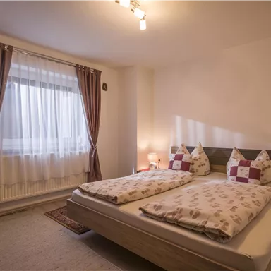 Ein gemütliches Schlafzimmer mit zwei Betten, hellen Vorhängen und einem Fenster. Es gibt sanfte Beleuchtung und dekorative Kissen.