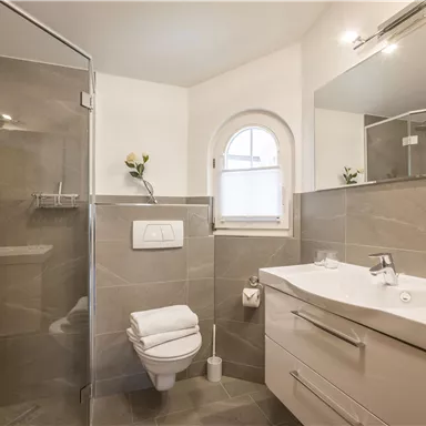 A modern bathroom with a shower and a large mirror. The walls are in neutral gray tones.