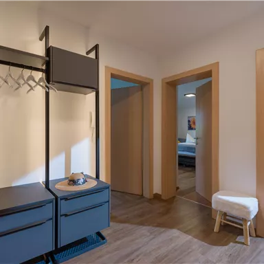 A bright hallway with a modern coat rack and a small table. In the background, two open doors to additional rooms are visible.