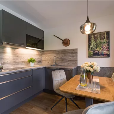 A modern kitchen with dark cabinets and a cozy dining area. The table is decorated with flowers and a rustic picture.