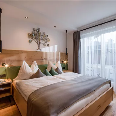 A modern bedroom with a comfortable double bed and wooden furniture. Large windows ensure plenty of light and a beautiful view outside.