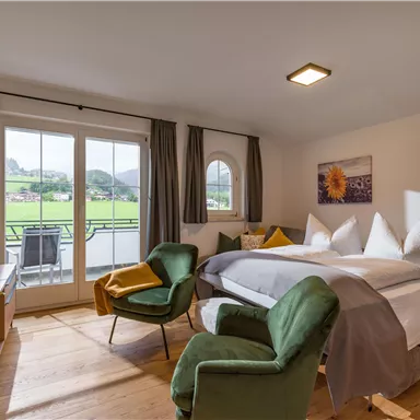 A bright room with a large bed, two cozy armchairs, and a balcony that offers a beautiful view of the countryside. The decor is modern and inviting.