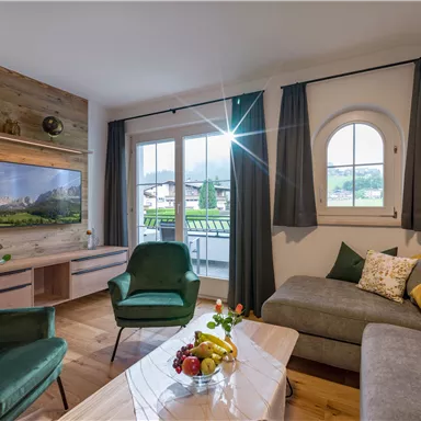 A cozy living room with modern furniture and a large window. The room is bright and friendly, with a beautiful view outside.
