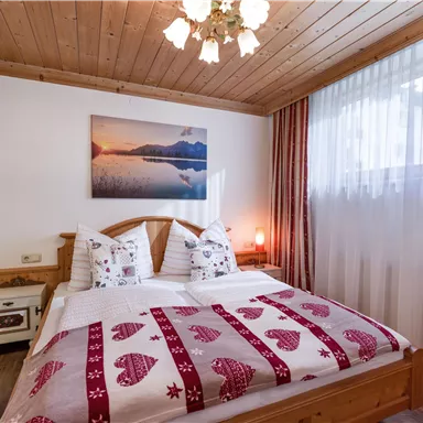 Ein gemütliches Schlafzimmer mit einem Doppelbett und einem Holzdecke. Das Zimmer ist hell mit einem Fenster, Vorhängen und einem schönen Wandbild.