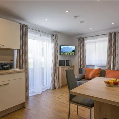 Eine helle und moderne Wohnung mit einer offenen Küche und einem gemütlichen Wohnbereich. Der Raum ist mit einem Esstisch, bequemen Stühlen und einem Fernseher ausgestattet.