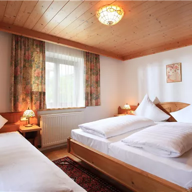 A cozy bedroom with two beds and a warm wooden ceiling. Bright windows and a carpet add an inviting touch to the atmosphere.