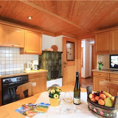 A cozy kitchen with wooden cabinets and a table with a fruit basket. A television and a pleasant atmosphere create an inviting ambiance.