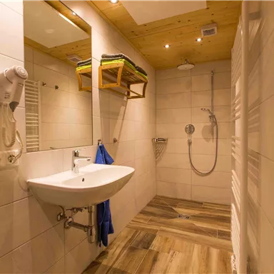 A modern bathroom with a shower and a sink. The walls are tiled and there are wooden panels on the ceiling.