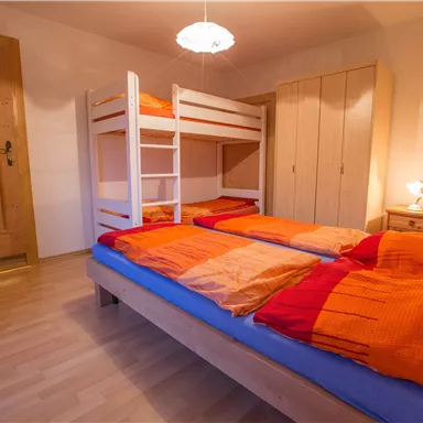 A cozy bedroom with a bunk bed and two single beds. The room has a warm wood tone and is well-lit.