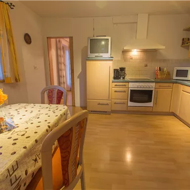 A bright and cheerful kitchen with wooden cabinets and modern appliances. On the table, there is a small floral decoration.