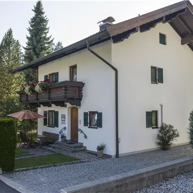 A beautiful house with a balcony and green shutters. Surrounded by trees and a well-kept garden.