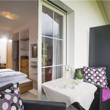 A cozy balcony with a small table and two chairs. In the background, you can see a bright room with a modern furnishing style.