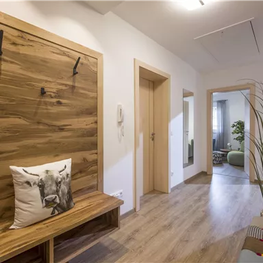 A bright hallway with wooden furniture and a cozy bench. Some hooks hang on the wall, and there is a small plant accent.