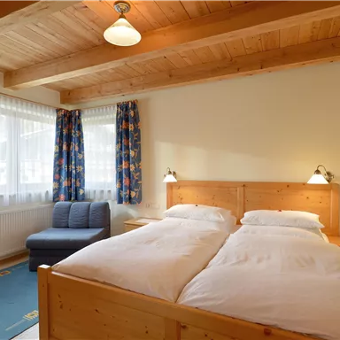 Ein gemütliches Zimmer mit zwei Betten und Holzdetails. Die große Fensterfront sorgt für viel Tageslicht.