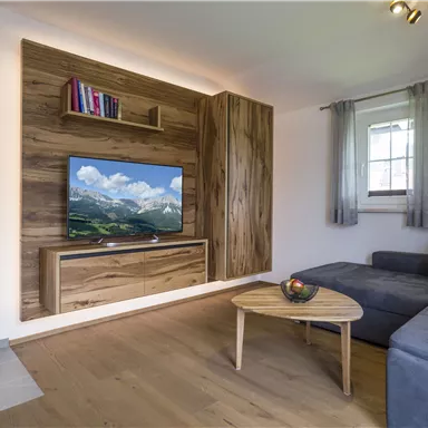 A cozy living room with a TV and wood paneling. Next to the sofa, there is a fireplace and a small coffee table.