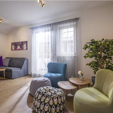 A modern living room with comfortable furniture and large windows. There is a plant-like accent and stylish side tables.