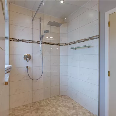 A modern shower with bright tiles and a large showerhead. The space is clean and well lit.