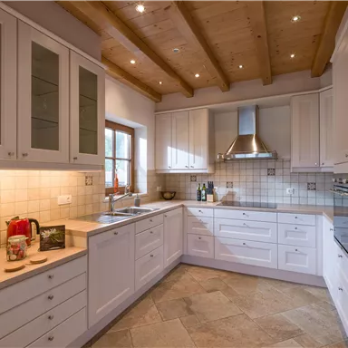 A modern kitchen with white cabinets and stone flooring. The lighting creates a bright and inviting atmosphere.