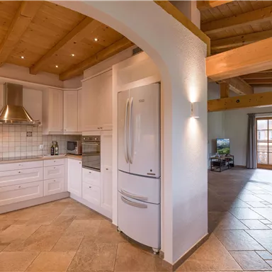 A modern kitchen with bright cabinets and a large refrigerator. The space is open and leads to a cozy living area.