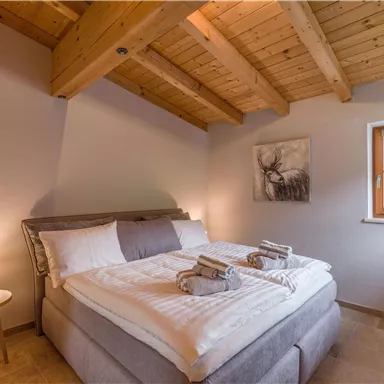 A cozy bedroom with a large bed and wooden ceilings. The room is brightly lit and has a window with a view outside.