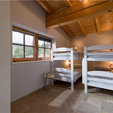 A cozy bedroom with two bunk beds and a window that lets in daylight. The wooden ceiling gives the room a warm atmosphere.
