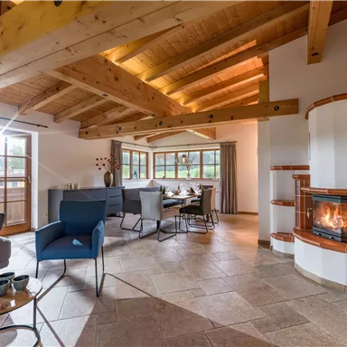 A modern living and dining room with bright wooden beams and large windows. A cozy fireplace creates an inviting atmosphere.