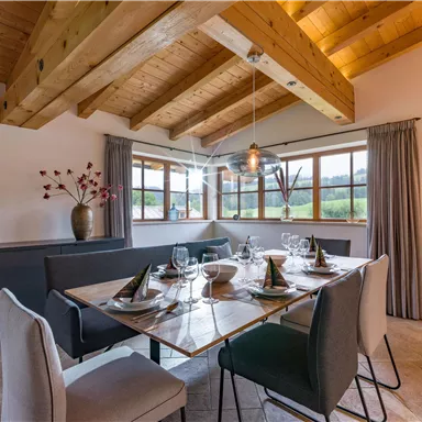 An elegant dining room with a large table and modern chairs. The large windows offer a beautiful view of nature and let in plenty of light.