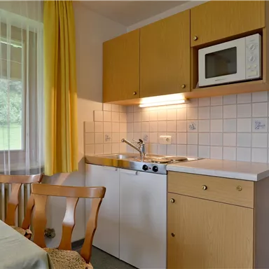 Eine gemütliche Küche mit hellen Schränken und einem Mikrowellenofen. Der Tisch ist eingedeckt und es gibt einen Blick ins Grüne durch das Fenster.